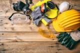 Construction safety. Protective hard hat, headphones, gloves and glasses on wooden background, copy space, top view