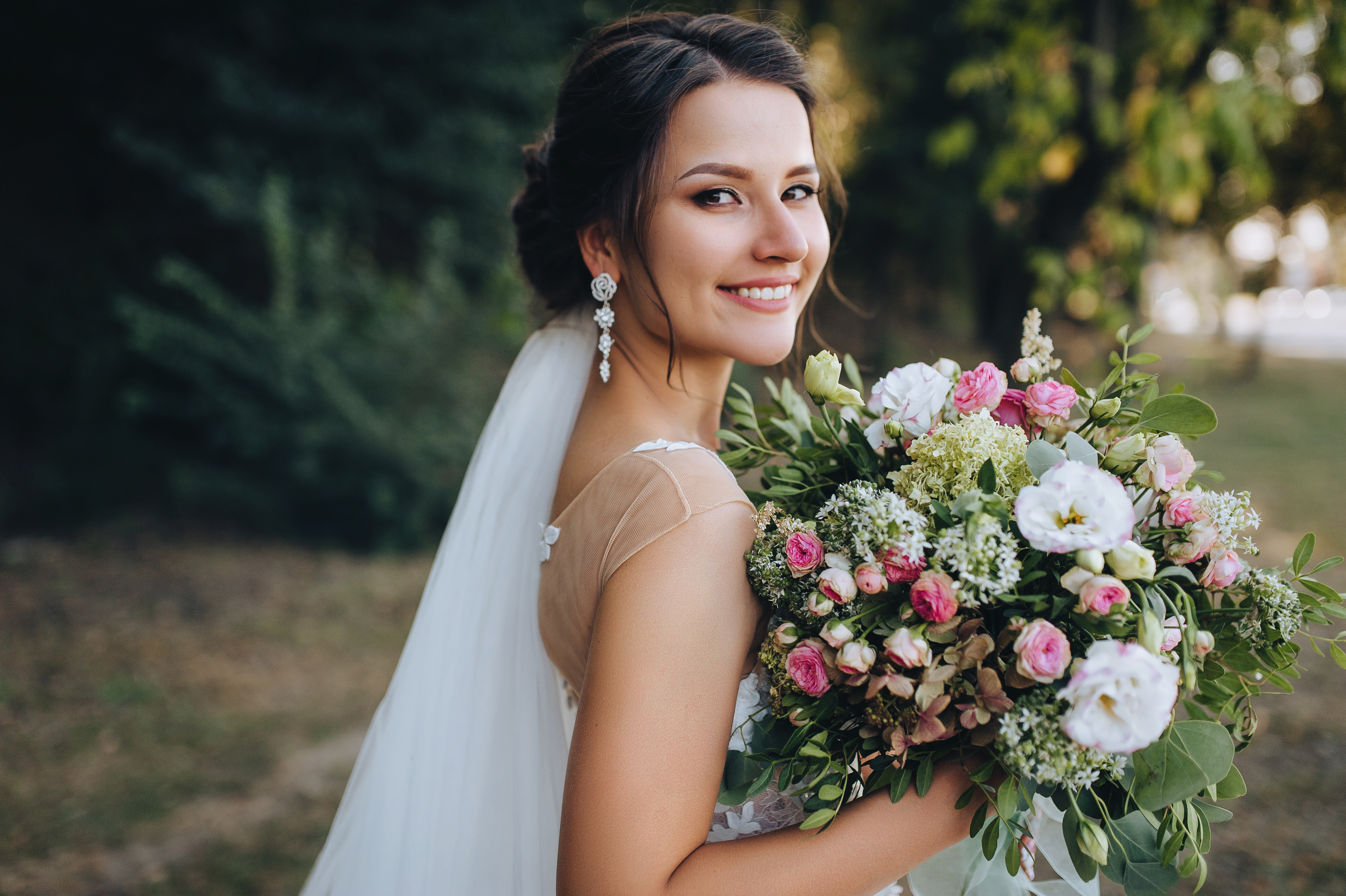 A beautiful bride stands on nature in greenery with a large bouquet. Wedding portrait close-up of the young bride. Wedding photography.
