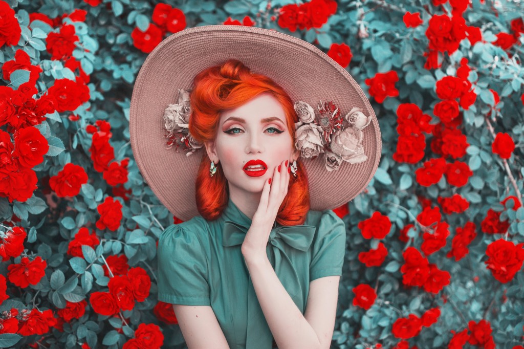 Valentines Day background. Fabulous retro girl with red lips in mint dress on awesome summer background. Woman portrait. Awesome redhead model expresses emotions on background of roses bush.